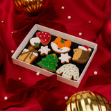 A Molly's Bakehouse gift box filled with decorated Christmas woodland themed mini iced biscuits, including a fox, Christmas tree, mushroom, snowflake, sweater, and hedgehog. Arranged on a red satin fabric with velvet bows and Christmas ornaments.