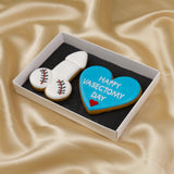 Two cookies in a box, one shaped like a willy and the other like a heart with 'Happy Vasectomy Day' text, on a beige fabric background.